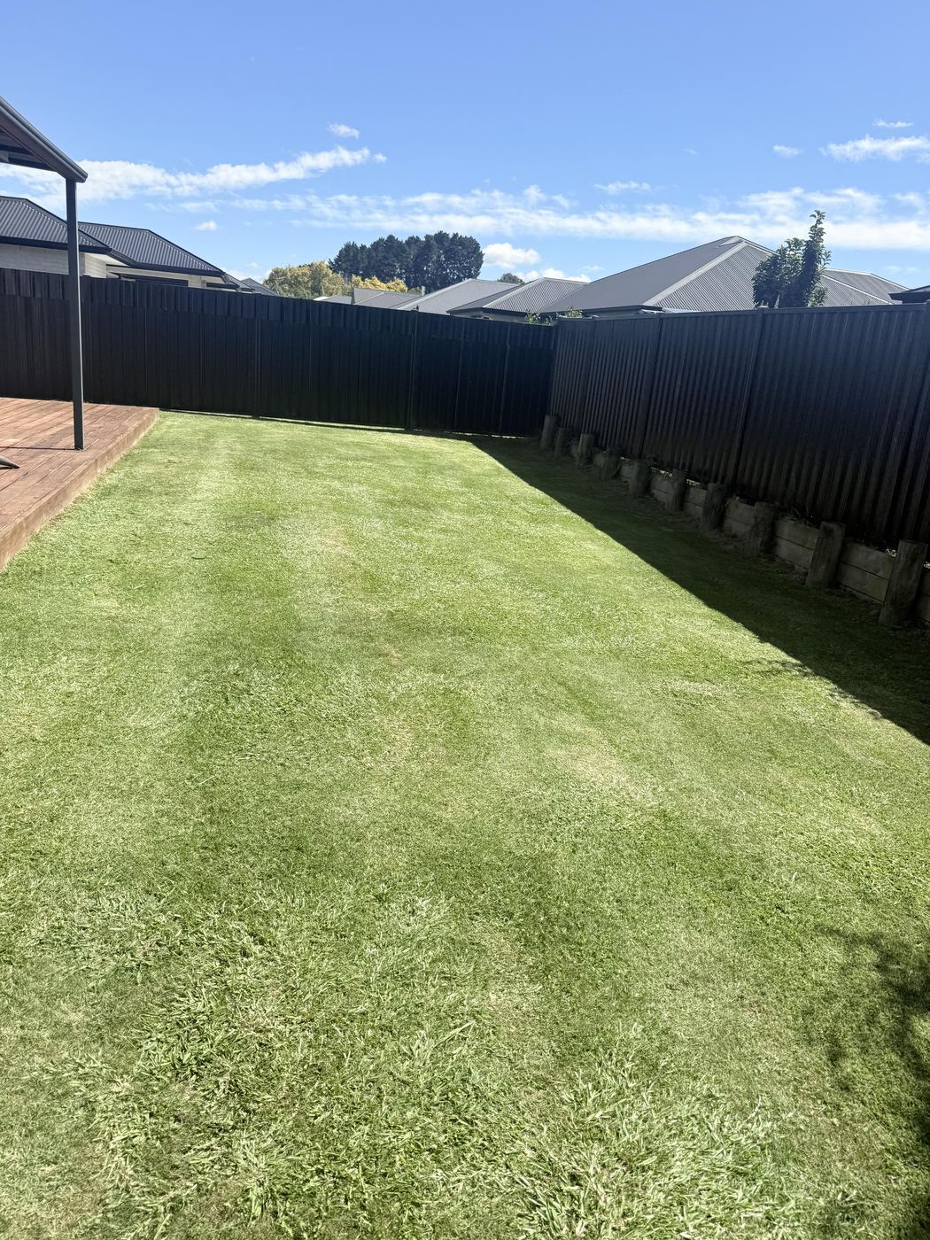 Backyard lawn mowed alongside a timber deck by JR Lawn Mowing